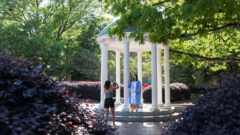 People taking photos at the Old Well in graduation regalia.