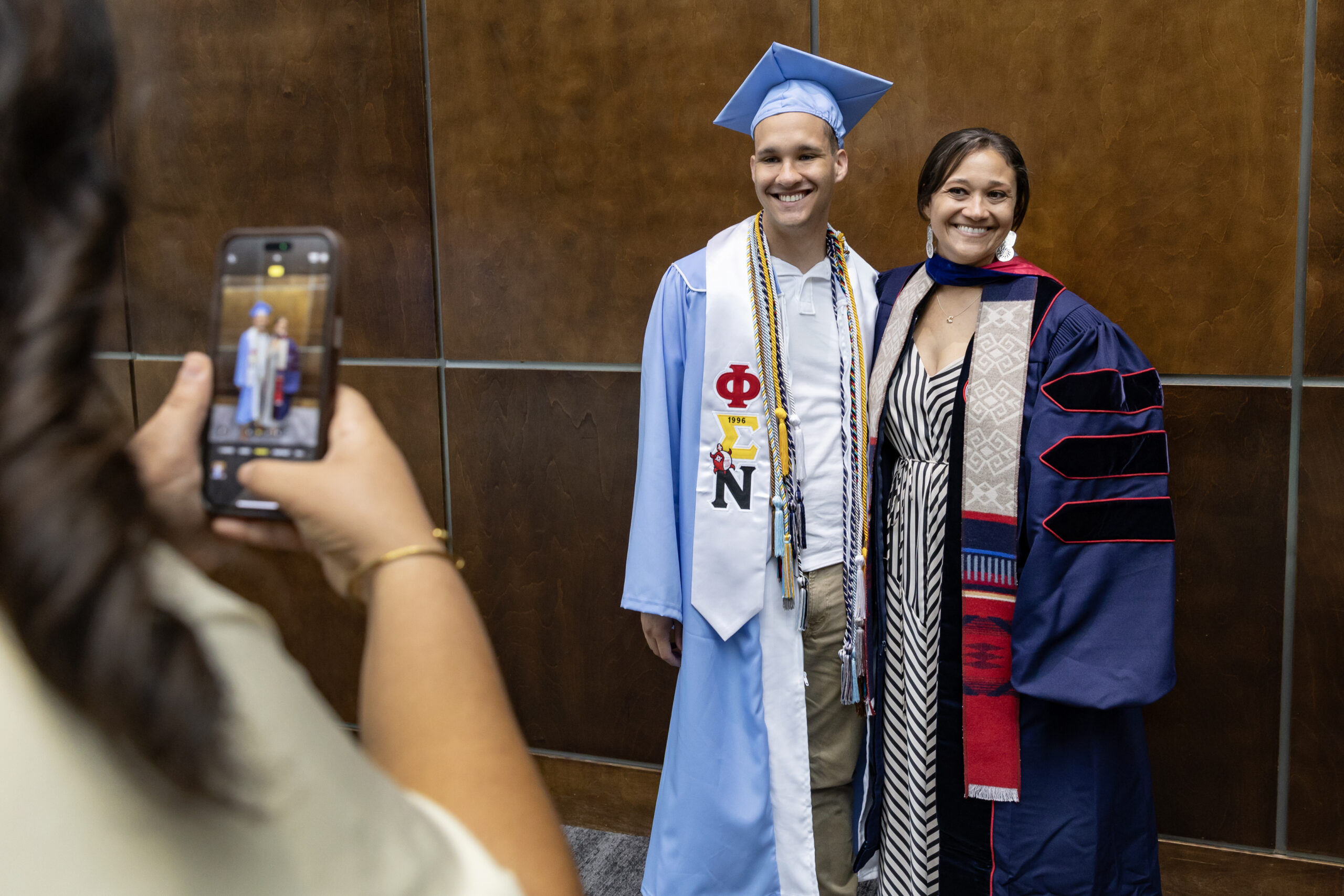 Students pose for a commencement photo while wearing doctoral regalia.